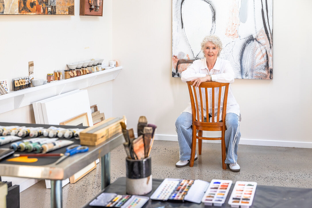 Lorna Crane seated in her studio with painting materials, watercolour palettes and works in progress