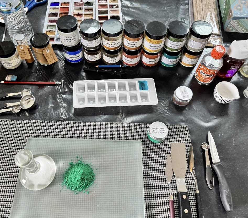 Pigment jars, watercolour palette, tools and ground turquoise pigment on a studio bench
